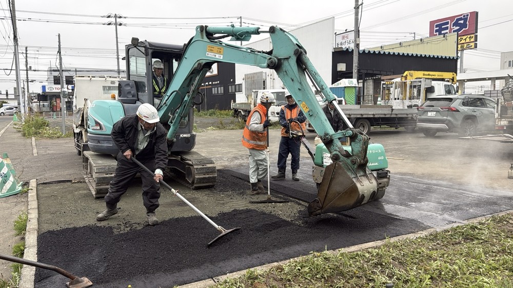 重機と作業員が舗装面を整えている様子